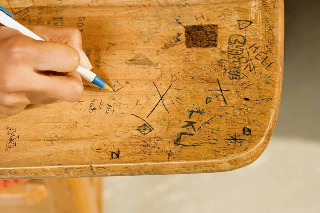 School student writing on desk for vandalism
